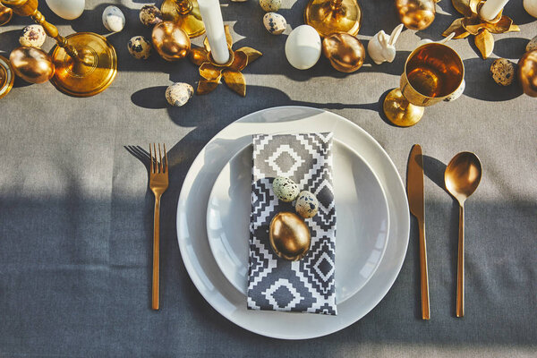 top view of golden egg and quail eggs on plates in restaurant, easter concept