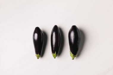 top view of three eggplants on white surface clipart