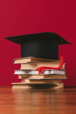 Academic cap on top of pile of books on red clipart