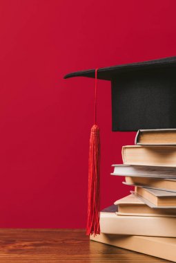 Cropped image of academic cap on pile of books on red clipart