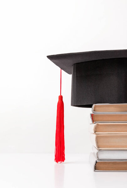 Cropped view of academic cap on pile of books isolated on white