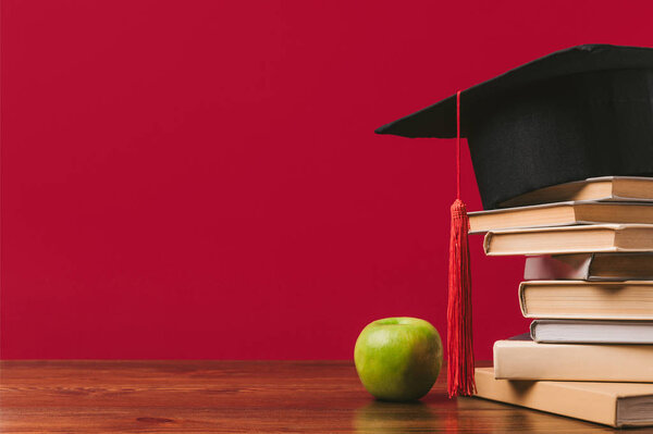 Cropped view of pile of books with academic cap on top and apple on red