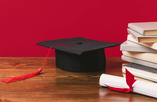 Cropped image of pile of books with diploma and academic cap on red