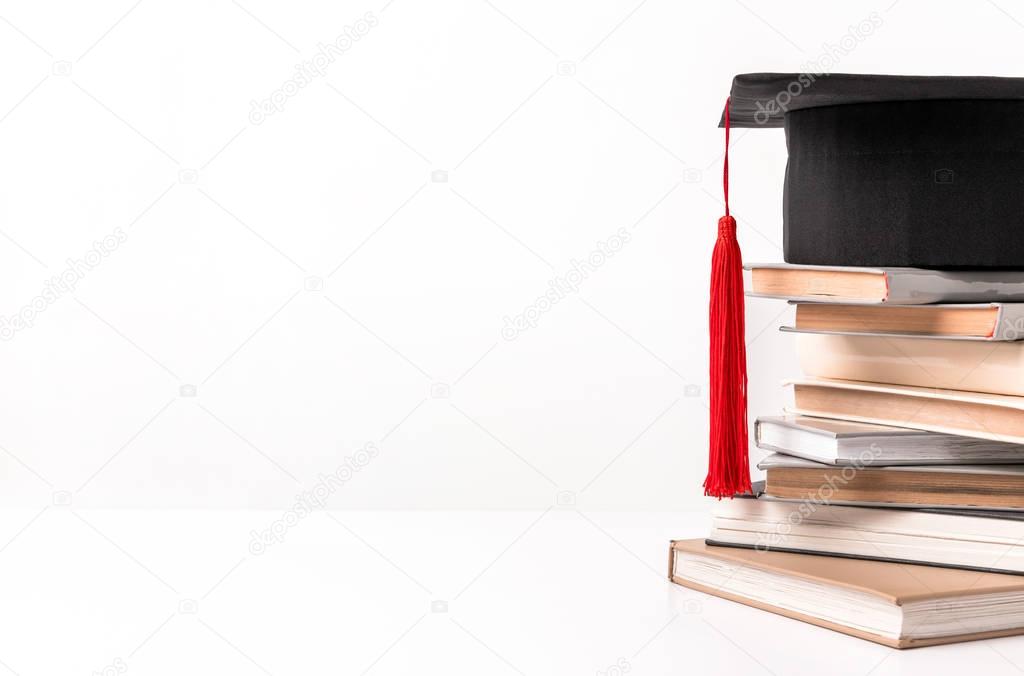 Cropped view of quare academic cap on stack of different books isolated on white 