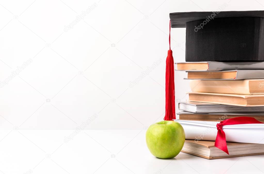 Academic hat on pile of books with diploma and apple isolated on white
