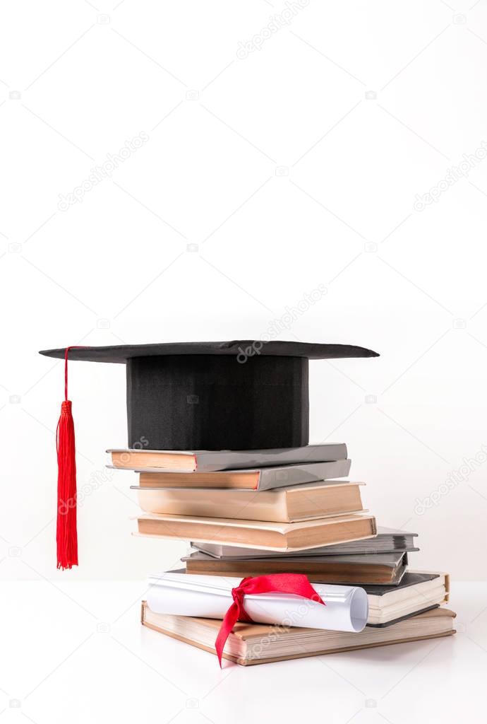 Academic cap on pile of books and diploma isolated on white