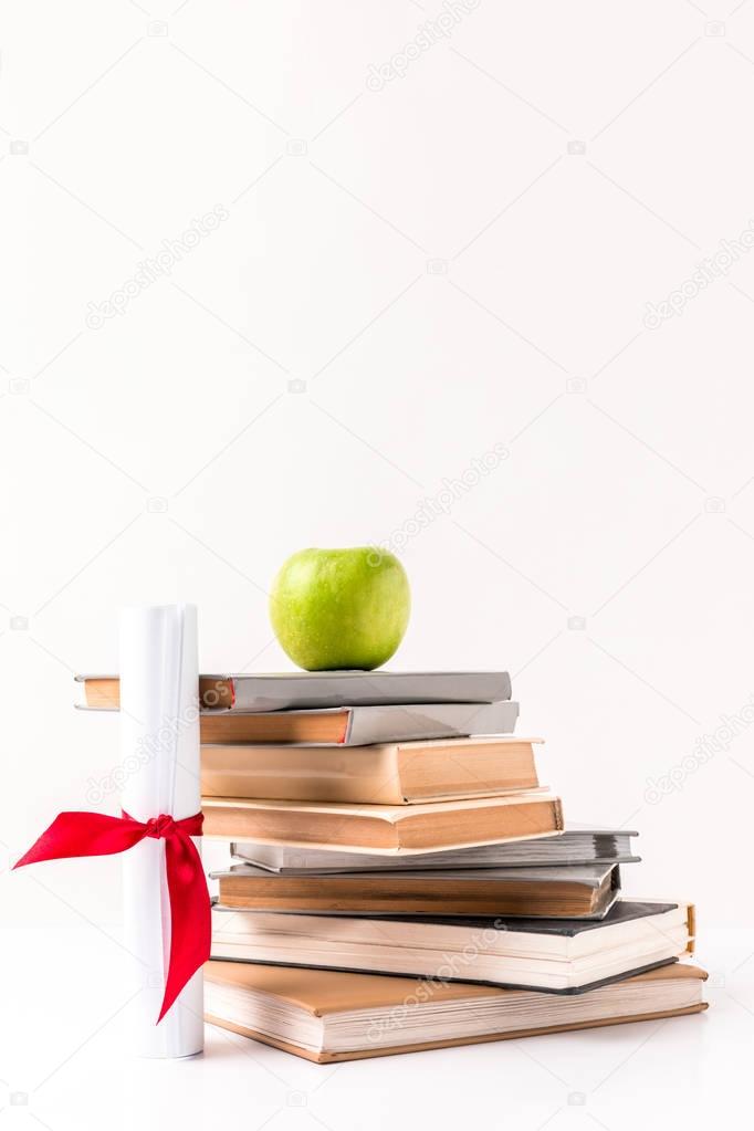 Diploma with stack of books with apple on top isolated on white