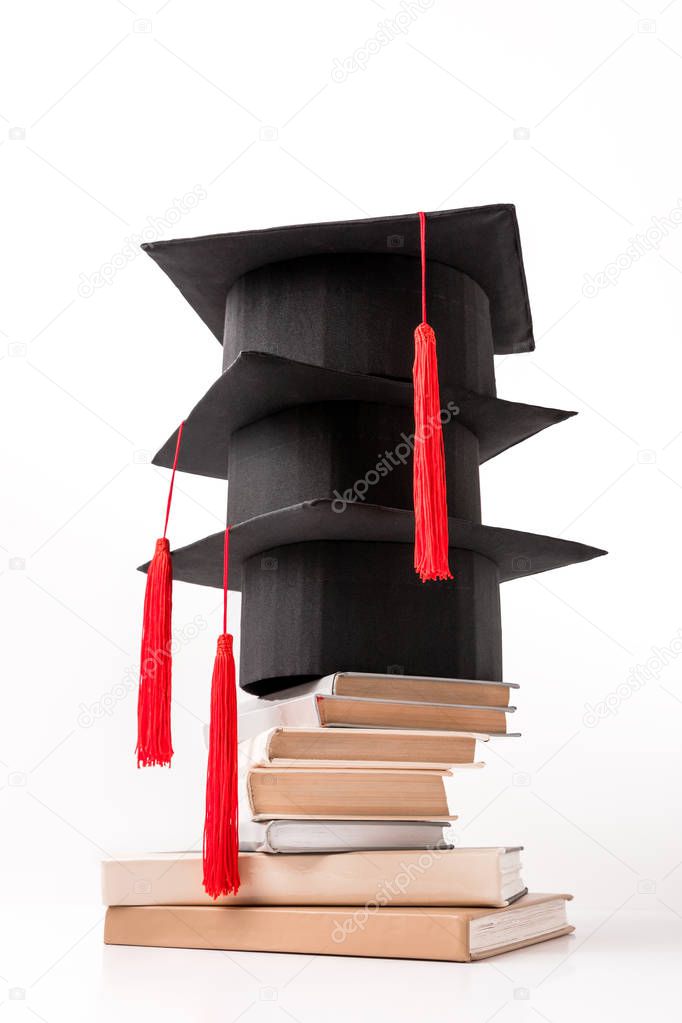 Square academic hats on pile of books isolated on white