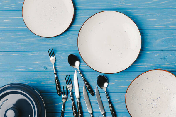 top view of plates with scattered forks, spoons and knifes on blue table