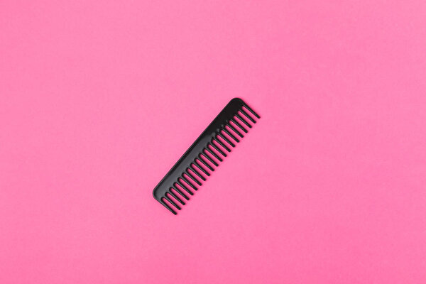top view of one black comb, isolated on pink