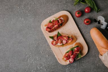 top view of tasty tomato bruschetta on wooden board and fresh ingredients on grey clipart