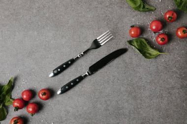 top view of fresh tomatoes, basil and salt with cutlery on grey  clipart
