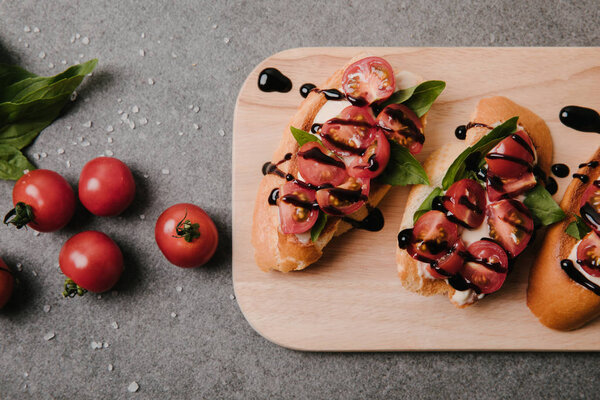 традиционная итальянская брускетта на деревянной доске, базилик и свежие помидоры на сером
    