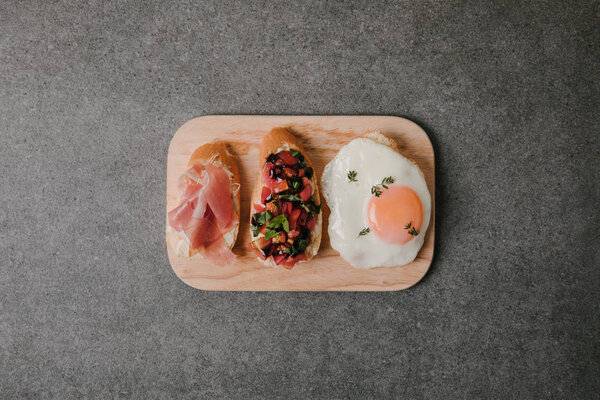 вид на вкусную антипасто брускетту с жареным яйцом на деревянной доске на сером
