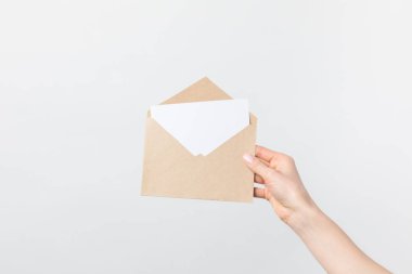 partial view of woman holding kraft envelope with blank card in hand isolated on white clipart