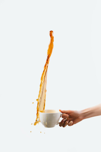 cropped view of hand holding big cup of coffee with splash, isolated on white