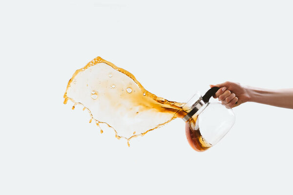 cropped view of hand holding glass pot with splashing coffee, isolated on white