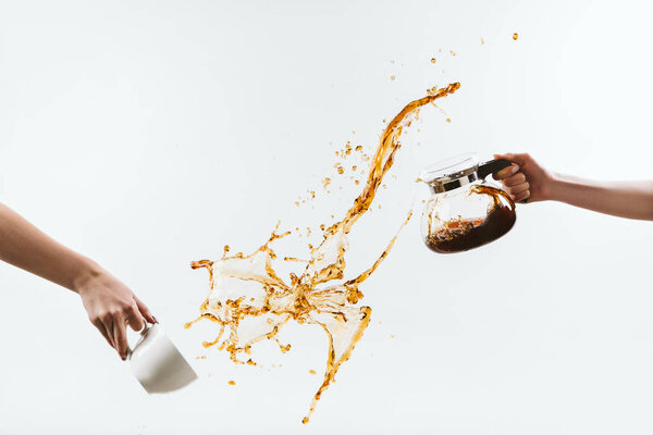 cropped view of hands splashing hot coffee from cup and glass pot, isolated on white