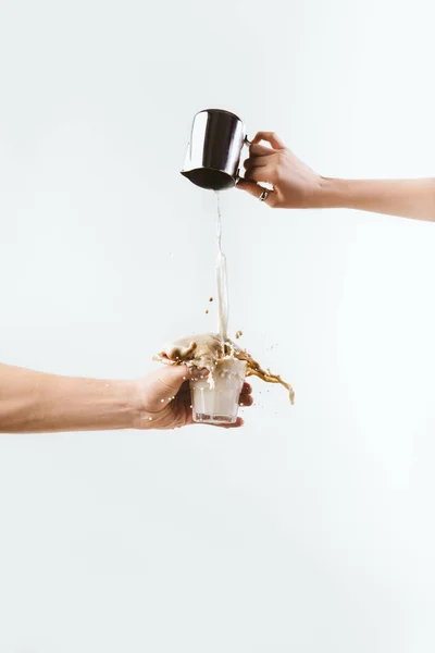 cropped view of hand splashing milk into glass of coffee, isolated on white