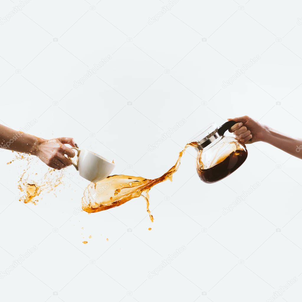 cropped view of hands splashing morning coffee from cup and glass pot, isolated on white