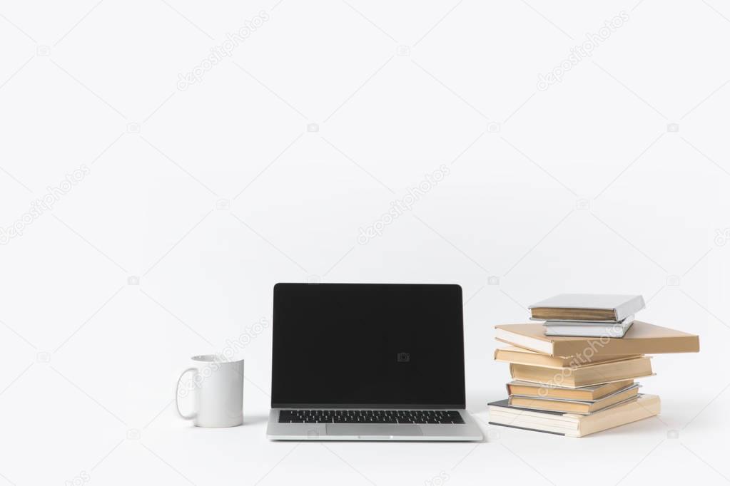 close up view of laptop with blank screen, mug and pile of books isolated on white