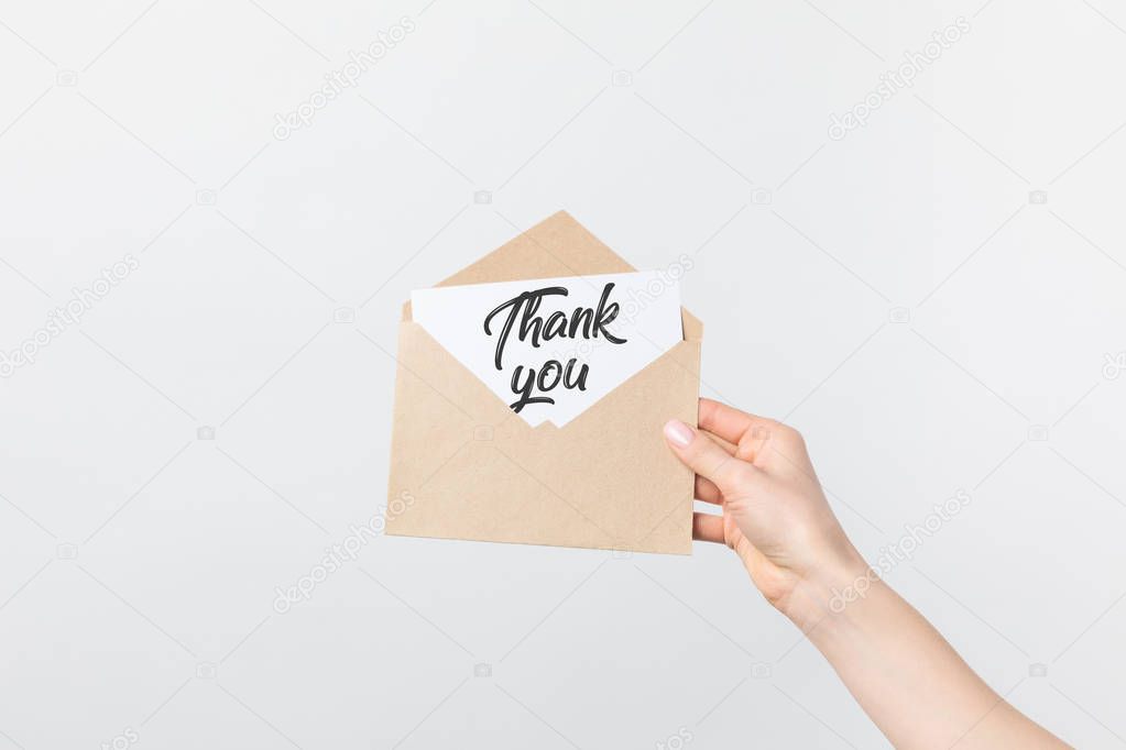 partial view of woman holding kraft envelope with thank you card isolated on white