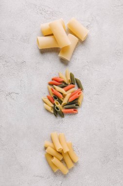 top view of piles of different raw pasta in row on concrete surface clipart