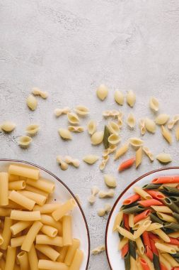 top view of various raw pasta in bowls on messy concrete tabletop clipart