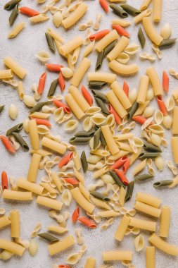 top view of various raw pasta spilled on concrete surface clipart