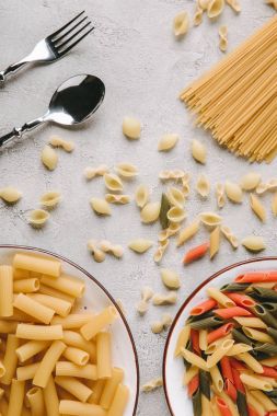 top view of various raw pasta and cutlery on messy concrete tabletop clipart