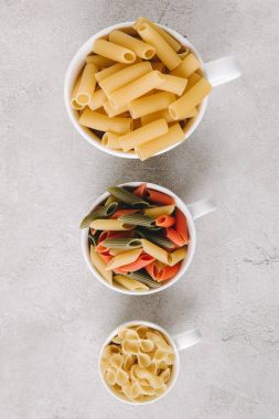 top view of various types of raw pasta in bowls standing in row on concrete tabletop clipart