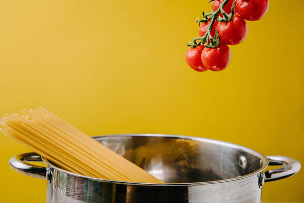 spaghetti boiling in stewpot with branch of cherry tomatoes above isolated on yellow
