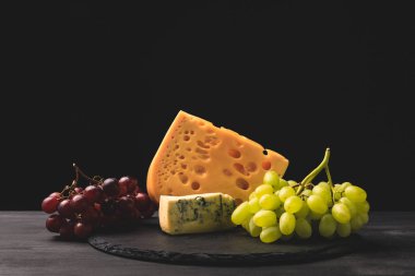 Blue cheese and emmental on board with grapes on black clipart