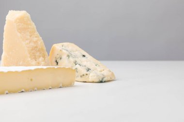 Close up view of brie, cheddar and blue cheese on gray  clipart