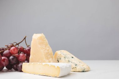 Closeup view of three types of cheese and grapes on gray 
