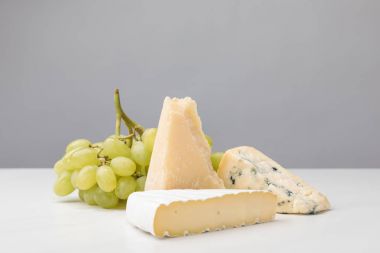 Closeup view of three types of cheese and grapes on gray  clipart