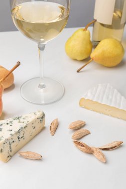 Closeup view of brie and blue cheese with almond, pears, wine glass, bottle and baguette on gray  clipart