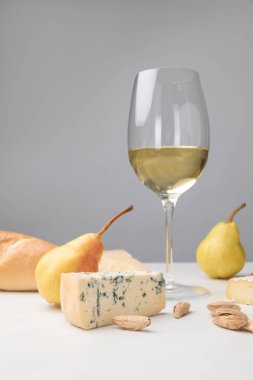 Close up view of dorblu cheese, wine glass, pears, almond and baguette on gray clipart