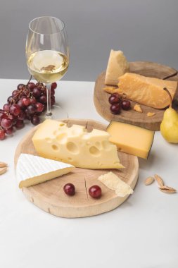 Elevated view of different types of cheese on wooden boards, almond, wine glass and fruits on gray  clipart
