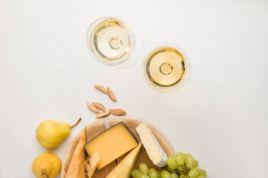 Top view of different types of cheese on wooden board, wine glasses, almond and fruits on white clipart