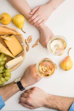 Top view of couple with wine glasses, different types of cheese, pears, grapes and almond on white  clipart