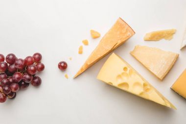 Top view of different types of cheese and grapes on white 