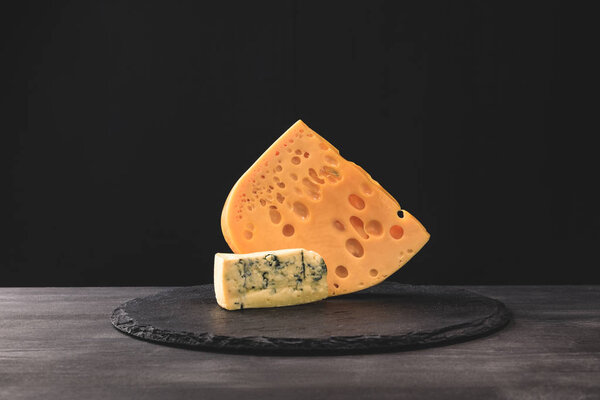 Closeup view of emmental and blue cheese on board on black 