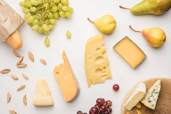 Top view of different types of cheese, grapes, pears, almond and baguette on white 