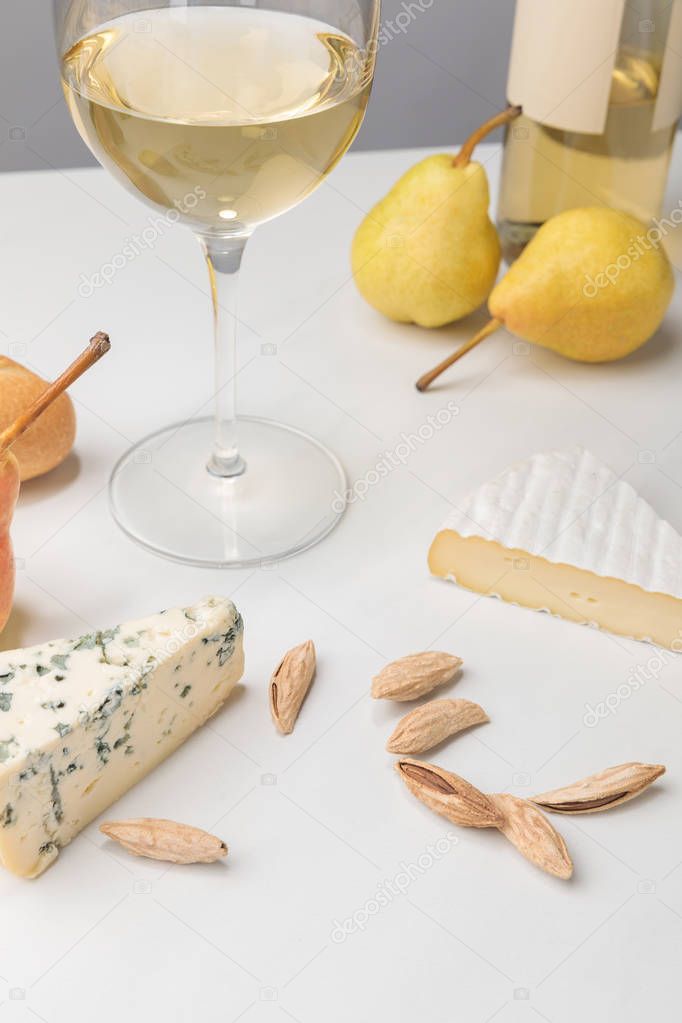 Closeup view of brie and blue cheese with almond, pears, wine glass, bottle and baguette on gray 