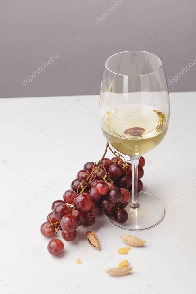 Closeup view of white wine glass, grapes and almond on gray