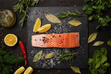 Raw salmon with herbs and lemons on slate background clipart
