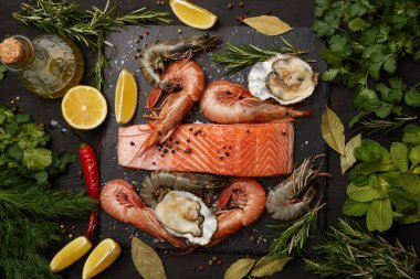 Raw salmon and assorted seafood with herbs and lemons on dark background