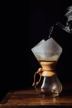 Hot water pouring into chemex with filter cone on wooden table  clipart