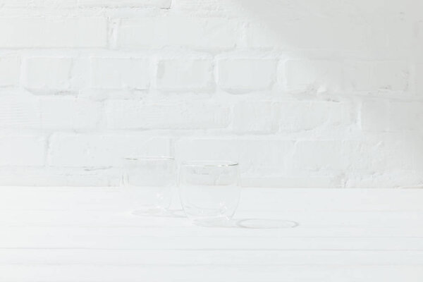 Front view of two empty glass mugs with brick wall behind 